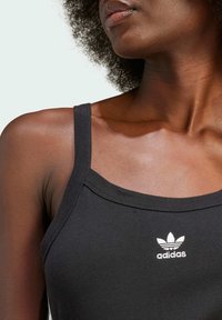 Canottiera sportiva nera con spalline sottili, dotata di un logo adidas ricamato bianco sul petto e una texture liscia e aderente.