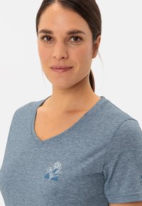 Modré melírované tričko s V-výstřihem vyrobené z jemné tkaniny, s malým bílým květinovým vzorem na levé části hrudníku.