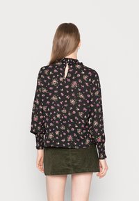 Blusa nera a fiori con scollo arricciato, caratterizzata da motivi floreali rosa e verdi. Dettaglio a chiusura a chiave sul retro e maniche lunghe con polsini arricciati.