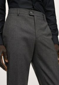 Graue maßgeschneiderte Hose mit flachem Bund, einzelner Knopföffnung und strukturiertem Stoff. Schmale Passform, mit seitlichen Taschen und Gürtelschlaufen.