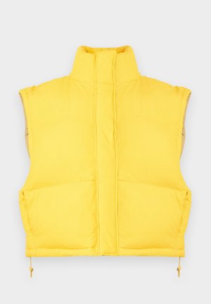 Geltonas pūkinis liemenė su aukšta apykakle, priekiu su užtrauktuku, šoninėmis kišenėmis ir reguliuojamu apačios raišteliu. Minkšta medžiaga su lygiu paviršiumi ir paminkštinimu.