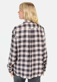 Geruite blouse in lichtroze en donkergrijs. Heeft lange mouwen, een kraag en een rugplooien voor bewegingsvrijheid. Gladde stoftextuur.