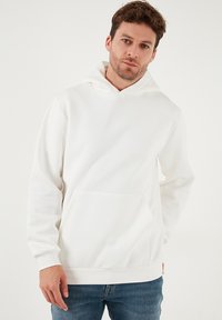 Valkoinen huppari, joka on valmistettu pehmeästä kankaasta. Siinä on edessä kengurun tasku ja säädettävä kiristysnauhallinen huppu. Varustettu resoreilla hihansuissa ja helmassa.