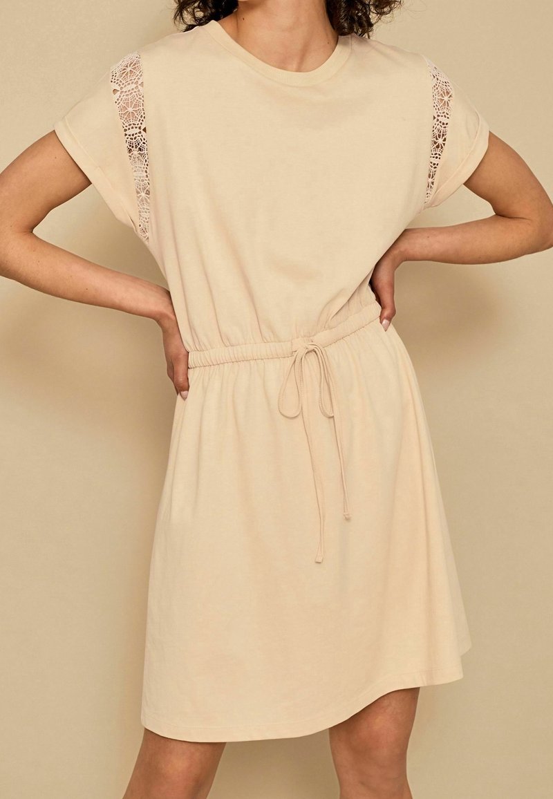 Robe en coton beige à manches courtes, dotée de détails en dentelle sur les épaules et d'une taille élastique à cordon pour un ajustement modulable.