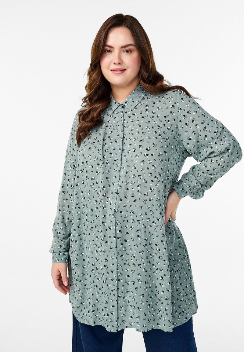 Light green button-up shirt with a collar, featuring a small floral pattern. Long sleeves, relaxed fit, and slightly rounded hem.