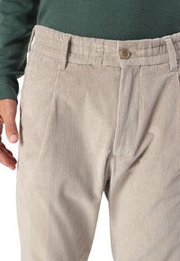 Beige manchesterbyxor med ett strukturerat vertikalt randmönster, med resårmidja och en knappstängning.