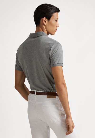 Pelēks polo krekls ar īsām piedurknēm, plakanu apkakli un ribām manžetēs, kopā ar baltām biksēm un brūnu jostu ar teksturētu detaļu.