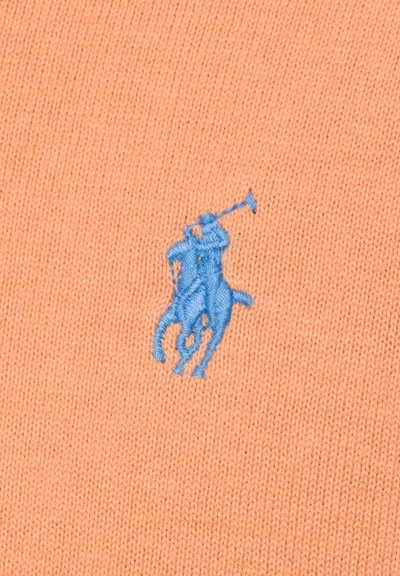 Blau bestickter Polospieler mit erhobenem Schläger auf pfirsichfarbenem, gestricktem Stoffhintergrund.