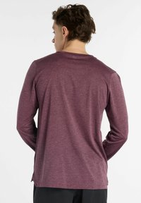 Long-sleeve shirt in a dark maroon color, made of a smooth fabric with a slight sheen. Features a round neck and side vents.