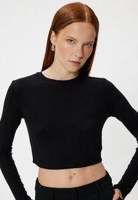 Zwart gekruist langslijfs shirt met een ronde halslijn, gladde textuur en aansluitende snit. Draagt met zwarte high-waisted broek.