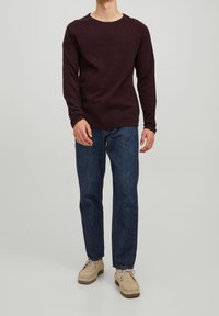 Chemise à manches longues bordeaux avec un col rond, associée à un jean en denim bleu et des chaussures beige, offrant une coupe décontractée et confortable.
