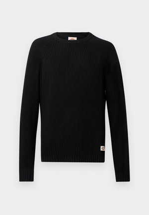 Svart, ribbestrikket genser med lange ermer og rund hals, med en liten logolapp nær kanten på en ensfarget bakgrunn.