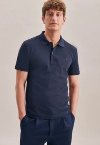 Granatowa koszulka polo z krótkimi rękawami, usztywnianym kołnierzykiem i subtelnym logo na piersi. Wykonana z miękkiego, lekkiego materiału.