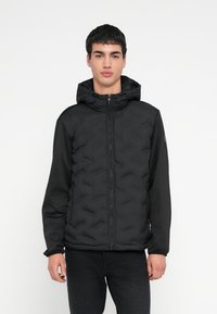 Svart dunjakke med quiltet design, har glidelåslukking og justerbar hette. Ermene er laget av et glatt materiale.