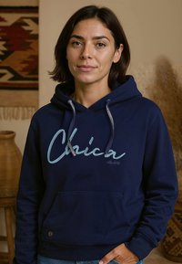Marineblauwe hoodie met een voorzak, voorzien van een grote geborduurde "Chica" in lichtblauwe schrift. Met trekkoorden en geribbelde manchetten.