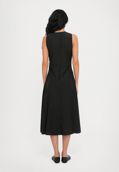 Black sleeveless dress with a fitted bodice and flared skirt, featuring a back zipper and smooth texture. Paired with black slip-on shoes.