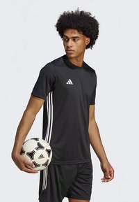 Must dõmm jersey lühikeste varrukatega, mille külgedel on kolm valget triipu. Mudel hoiab musta ja valge jalgpalli.