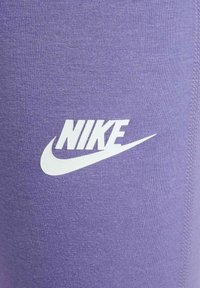 Leggings deportivos morados con una textura suave que presentan el logotipo de Nike en blanco. El diseño incluye una silueta ajustada y costuras sin costura.