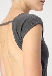 Hladký šedý top s krátkými rukávy a otevřeným designem na zádech. Materiál má texturovaný povrch s viditelnými švy.