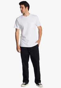 White cotton t-shirt with short sleeves and a left chest pocket, paired with black trousers and low-top sneakers. Simple, classic fit.