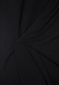 Černá tkanina s hladkou strukturou, která obsahuje zkroucený designový prvek vytvářející efektní volné dání. Jemný lesk zvýrazňuje vizuální hloubku.