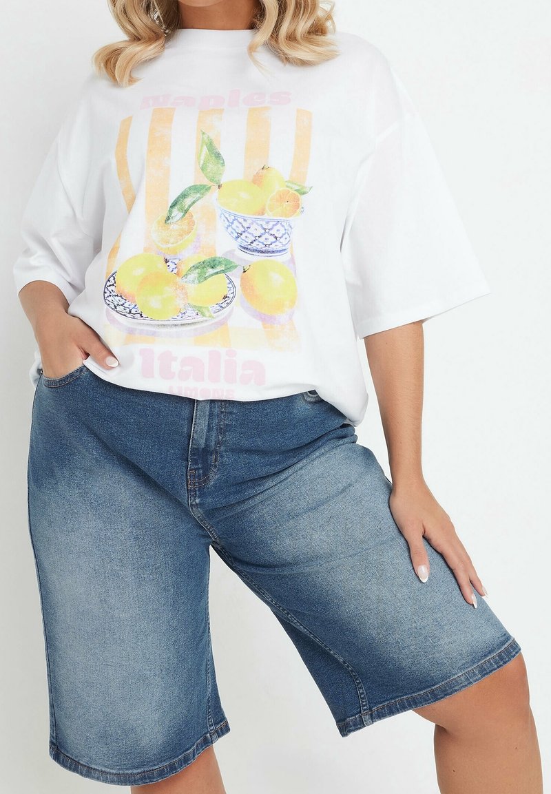 Maglietta bianca oversize con grafica colorata di limone e testo, abbinata a bermuda di jeans blu a vita alta. Tessuto dalla trama liscia.