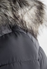 Zwarte pufferjack met een contrasterende nep-fur kraag. Glad, glanzend stof met een doorstikte textuur en opvallende stikseldetails.