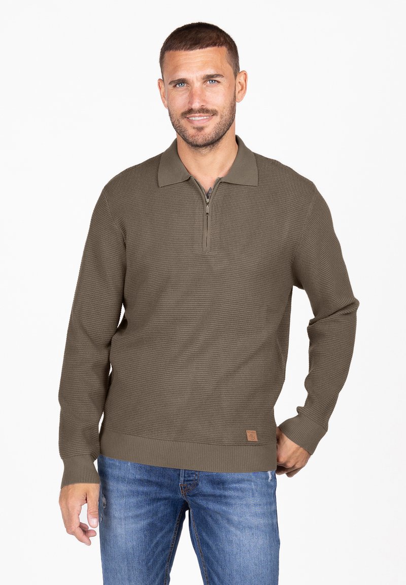 Olivgrüner Pullover mit langen Ärmeln und einem Viertel-Reißverschluss-Kragen, strukturiertem Strickdesign und einer kleinen Logo-Akzentierung unten links.