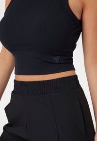Crni rebrasti crop top s širokim naramenicama i malom oznakom, uparen s visokim crnim hlačama sa elastičnom gumicom.