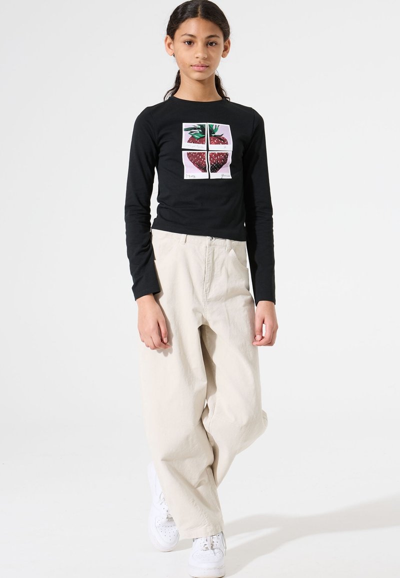 Schwarzes Langarmshirt mit einem Erdbeer-Graphic auf der Vorderseite, kombiniert mit lockeren beigen Hosen und weißen Sneakers.