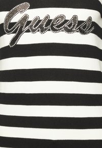 Pull noir et blanc à rayures avec un logo « Guess » en strass sur la poitrine et une finition texturée.