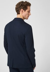 Navyblauer, maßgeschneiderter Blazer aus glattem Stoff, mit strukturierten Schultern, schlanker Passform und zwei Seitentaschen; verfügt über einen geschlitzten Rücken.