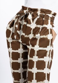 Bruine geklede broek met een crèmekleurig abstract ontwerp. Gemaakt van zachte stof, met een hoge taille, een strikceintuur en voorzakken.