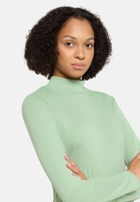 Langärmliges, hochgeschlossenes Oberteil in hellgrün, aus weichem Stoff mit schmaler Passform. Verfügt über eine glatte Textur und ein elegantes Design.