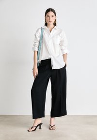 Λευκό πουκάμισο με μακρύ μανίκι και κουμπιά, μαύρες φαρδιές παντελόνες, μαύρες σандάλια με τακούνι και λουριά, και μια αδιάβροχη τσάντα σε ανοιχτό μπλε χρώμα με ρυθμιζόμενο λουρί.