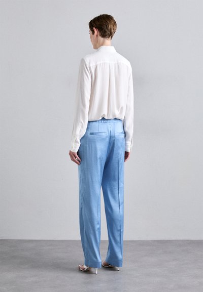 White long-sleeve blouse with buttons, paired with light blue, wide-leg trousers featuring an elastic waistband and back pockets.