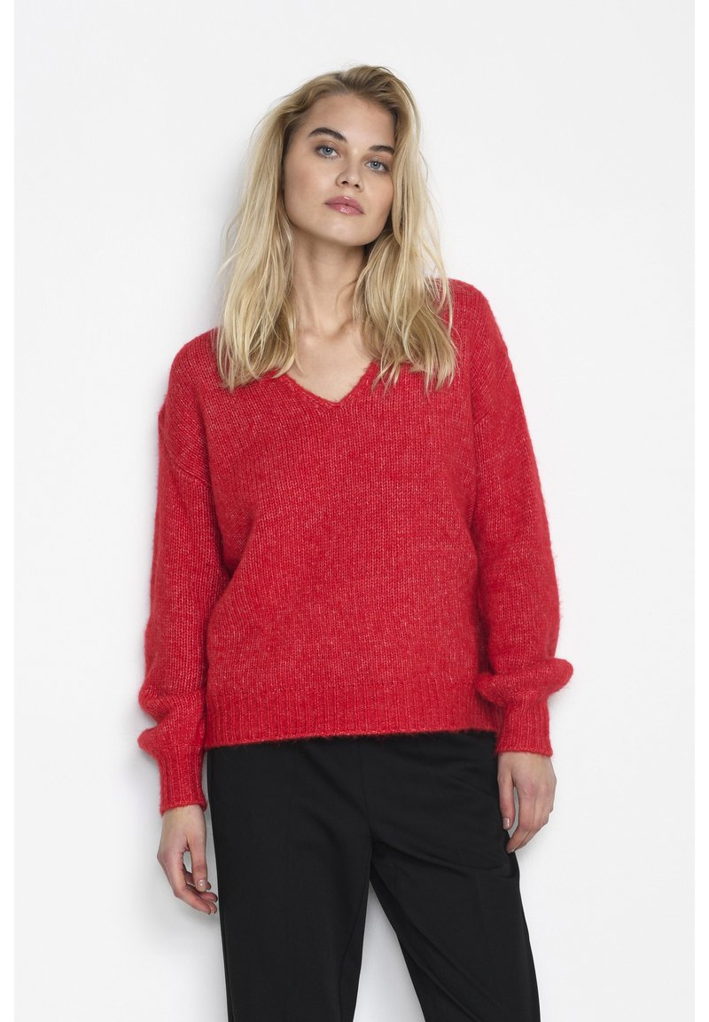 Roter, übergroßer Strickpullover mit V-Ausschnitt, der gerippte Bündchen und Saum aufweist. Trägt man mit schwarzen Hosen, die eine entspannte Passform und Textur betonen.