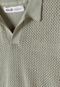 Polo en maille gris clair avec col ouvert et étiquette de la marque "minoti" visible indiquant la taille et l'origine.