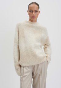 Cream-colored, fuzzy sweater with a high neckline and long sleeves, paired with light beige, pleated trousers. Soft, textured fabric.
