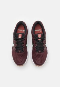 Une paire de chaussures de course Nike bordeaux avec des lacets noirs, un logo swoosh bleu clair et des semelles blanches, vue de dessus sur un fond blanc.