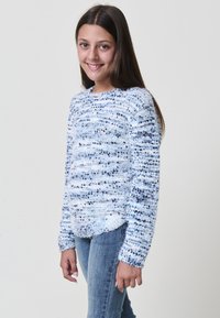 Maglione morbido blu chiaro con strisce blu di varie tonalità, scollatura rotonda e maniche lunghe. Indossato con jeans in denim. Texture soffice e vestibilità casual.