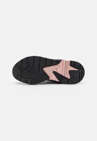 Schwarze Gummisohle eines Sneakers mit strukturiertem Grip, ausgestattet mit einem rosa Akzent im Mittelfußbereich und verschiedenen Profilmustern für besseren Halt.