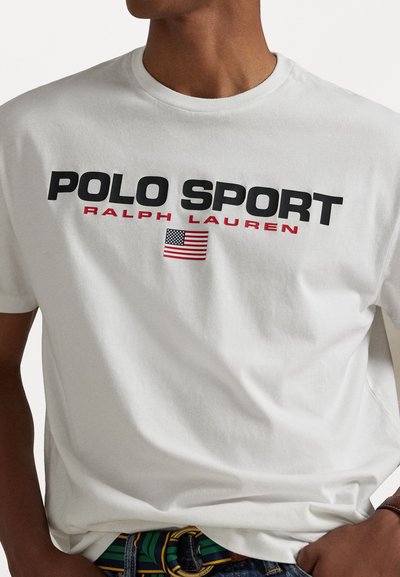 Tricou alb din bumbac cu text negru bold "POLO SPORT", "RALPH LAUREN" în roșu și un mic detaliu cu steagul american sub text.