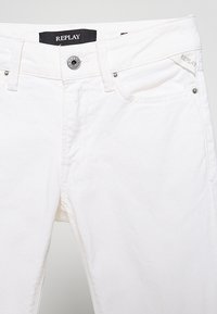 Jean en denim blanc avec fermeture par bouton et fermeture éclair, passants pour ceinture, poches avant et broderie discrète du logo de la marque sur la ceinture.