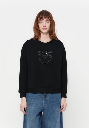 Felpa nera in cotone con un design testurizzato nero sul davanti, colletto rotondo e polsini a coste, abbinata a pantaloni in denim.