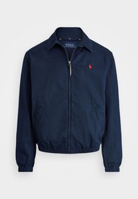 Dunkelblau leichte Jacke mit Reißverschluss, zwei Seitentaschen, elastischen Bündchen und einem kleinen roten Logo auf der linken Brust. Baumwollmischgewebe.