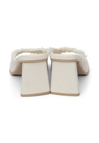 Beige Stoff-Pantoletten mit einem fransigen Obermaterial, offenem Rücken und einem chunky strukturierten Absatz. Glatte Sohle mit leichter Wölbung.