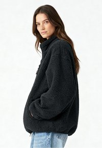 Veste polaire noire à enfiler avec col montant, poche zippée et coupe décontractée. Caractérisée par un tissu doux et texturé ainsi que des poignets élastiques.