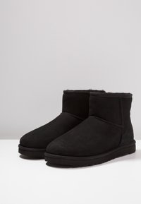Botas de tobillo de ante negro con punta redondeada, forro suave y suela de goma plana. Presenta costuras mínimas a lo largo de las costuras.