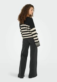 Gehaakte zwart-wit gestreepte sweater, lange mouwen, ontspannen pasvorm, gecombineerd met high-waisted zwarte wijde jeans. Getextureerde stof.